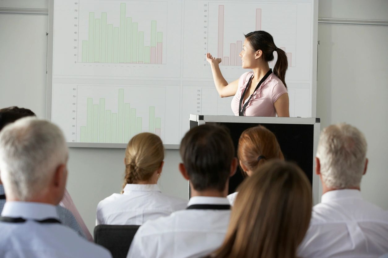 An audience watching a presenter at the front of a room