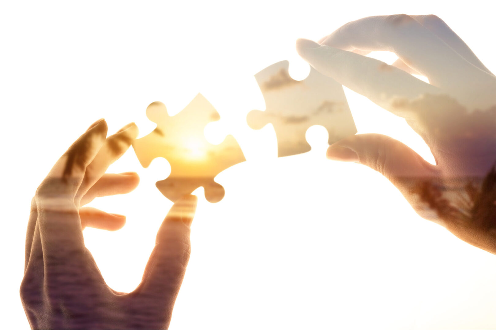 Two hands fitting puzzle pieces together in front of a sunset