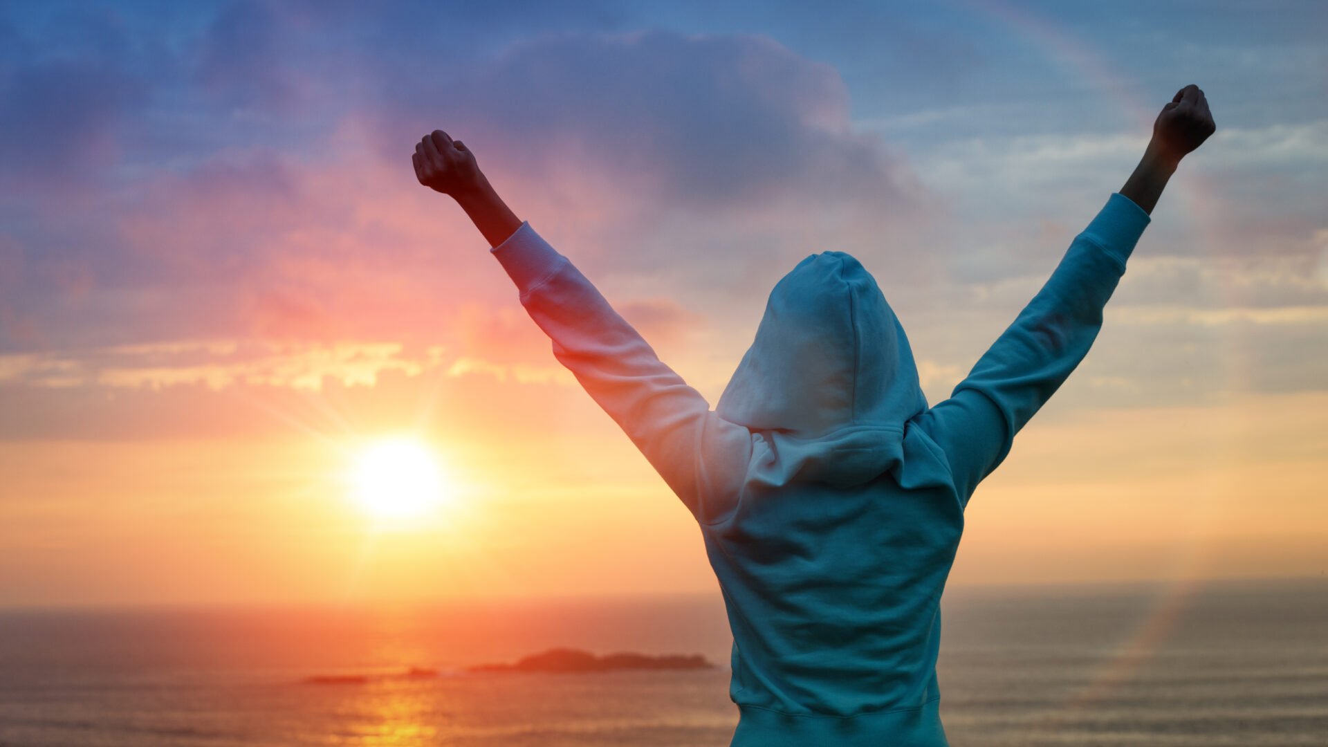 A person raising both arms toward a sunrise over the sea